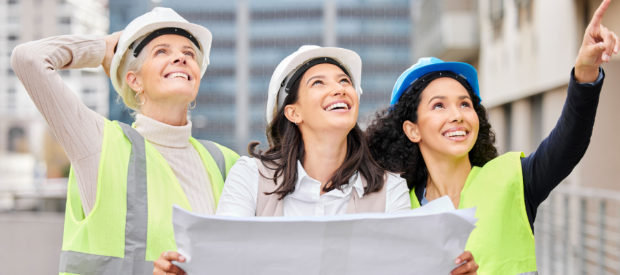 Trois femmes ingénieures en construction analysant un plan sur un chantier, portant des équipements de sécurité. "Les femmes dans les métiers du BTP".