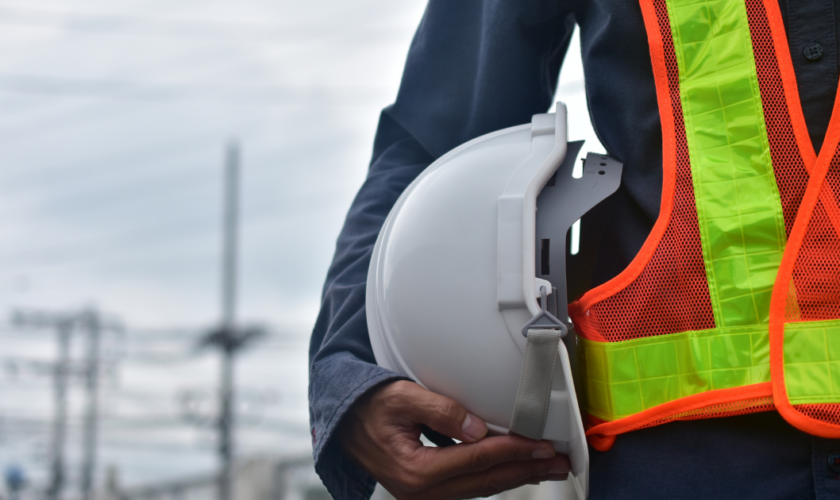Ingénieur sur chantier tenant un casque de sécurité, supervisant la construction d’un bâtiment.