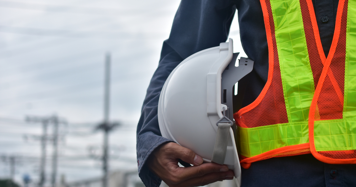 Ingénieur sur chantier tenant un casque de sécurité, supervisant la construction d’un bâtiment.